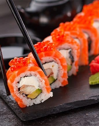 Lachs-Maki mit Ikura, gehalten von Stäbchen