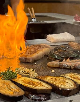 Flammen am Teppanyaki-Grill mit Fleisch, Garnelen und Gemüse